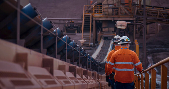Construction engineers walking alongside material conveyor belts at a mineral processing plant