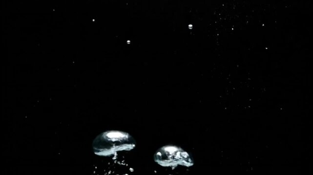 A captivating abstract video showcasing numerous bright, illuminated particles and bubbles elegantly floating, rising, and shimmering against a stark, deep black background. The various sizes and gent