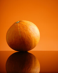 Harvest pumpkin reflecting on glossy surface creates a warm, inviting autumn mood, perfect for seasonal designs and fall recipe promotions