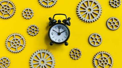 Time machine concept: Small black alarm clock surrounded by scattered wooden gears on a vibrant...