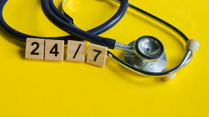 Stethoscope with 24/7 wooden blocks, symbolizing constant healthcare availability, emergency service, and continuous medical support on a bright yellow background.