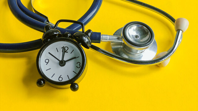 Stethoscope wrapped around an alarm clock, symbolizing the urgent need for health checkups, time for healthcare, and critical medical deadlines on a bright yellow background.