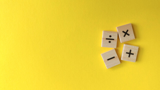 Fundamental arithmetic operation symbols on scattered wooden blocks against a vibrant yellow background with copy space.