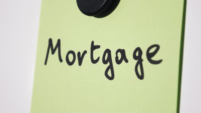 Pan reveal of Mortgage text on green note held by magnet on whiteboard with selective focus