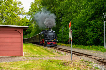 Zittauer Schmalspurbahn im Fr&uuml;hling auf der Fahrt durch das Zittauer Gebirge.
Dampflok 99 758 zieht historische Wagen durch gr&uuml;ne Landschaft und nostalgische Bahnh&ouml;fe in Sachsen