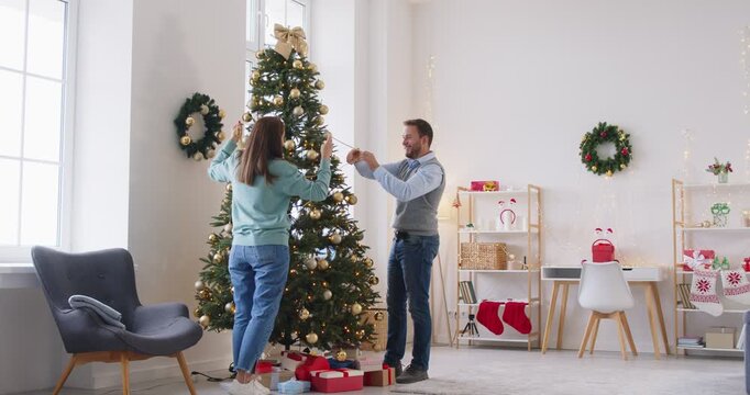 Decorating Christmas tree, Happy New Year family holiday at home, parents and small kids, holding xmas balls seasonal preparation, enjoying winter holidays together, present box near Xmas firtree