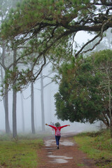 A woman is happily walking through a misty mountain forest along the path.