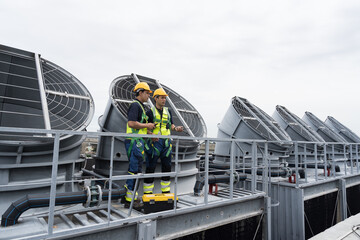 Naklejka premium Induced draft cooling towers. Male engineer or technicians maintenance and repair of cooling towers on rooftop of building, wearing safety uniform, helmet and handyman tools