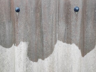 Gray textured background, wavy slate fence in the rain with two fasteners. A close-up view of a corrugated surface with visible rust and two black bolts. 