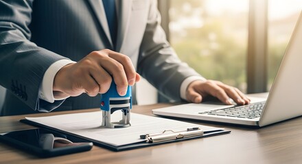 Business professional stamping document with laptop nearby in office setting