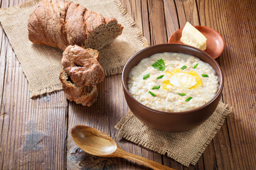 Oatmeal with green onions in ceramic bowl with wooden spoon and butter in a plate on wooden table. A sample for designers