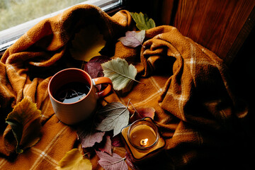 Cozy autumn still life with candle, orange plaid and fallen leaves.