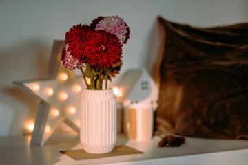 Soft candlelight and autumn leaves frame pink dahlias in vase on wooden surface. Cozy home atmosphere.