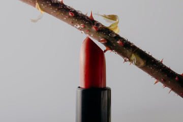 Red lipstick pierced by rose stem with thorns, breaking its surface. Bold creative macro beauty concept.