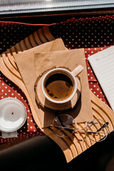 Small pink coffee cup with foam on sunny windowsill, surrounded by glasses, candle, and cozy decor.