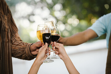 Close-up of friends clinking glasses of beer and wine during an outdoor barbecue party, celebrating and enjoying good times together.