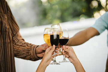 Close-up of friends clinking glasses of beer and wine during an outdoor barbecue party, celebrating and enjoying good times together.