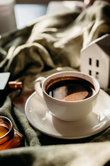 Cozy morning coffee scene with white cup and saucer on green plaid in golden sunlight.