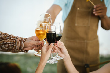 Close-up of friends clinking glasses of beer and wine during an outdoor barbecue party, celebrating and enjoying good times together.