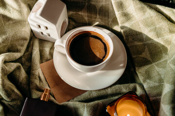 Morning coffee in white cup on green plaid, sunlit scene with candlelight and home coziness.