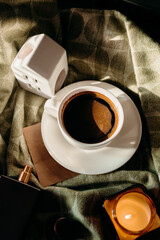 White cup and saucer with coffee on green plaid in sunlight, candle nearby. Cozy morning mood.