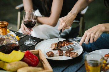 Close-up of friends clinking glasses of beer and wine during an outdoor barbecue party, celebrating and enjoying good times together.