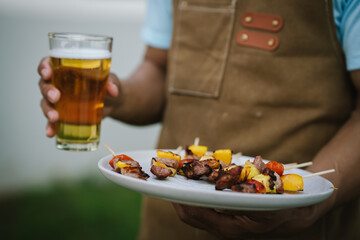 Close-up of grilled meat, potatoes, and vegetables cooking on a barbecue grill with smoke rising, showing delicious outdoor food preparation.