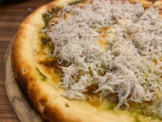 釜揚げしらすがたっぷりと乗せられた和風アレンジのピザのクローズアップ写真木のプレートの上に置かれた焼き目のついた生地がおいしそう