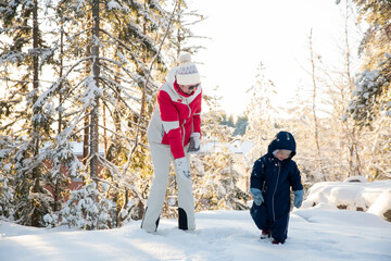 Naklejka premium Healthy grandmother and toddler play in snowy forest, tossing snow, enjoying golden winter light, family bonding, and active outdoor fun.