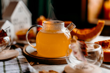 Cozy autumn still life with pumpkin tea, steaming teapot, candles and colorful leaves. Warm fall home mood.