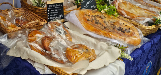 Traditional Spanish pastries wrapped in plastic are displayed in wicker baskets at a market stall, including sweet breads with chocolate and cream. Local food