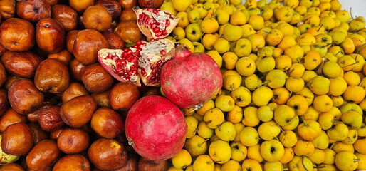 A colorful market display shows ripe jujubes on the left, bright yellow quinces on the right, and fresh pomegranates with seeds in the center. Fresh fruit