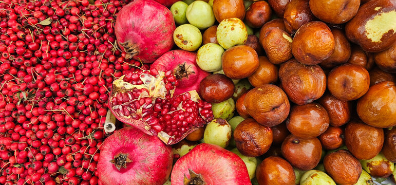 Fresh pomegranates, hawthorn berries, jujubes, and guavas are displayed together at a Spanish market, creating a colorful and vibrant fruit mix. Market fruits
