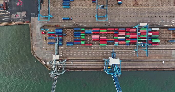 Busy industrial shipping ocean port with colorful freight cargo containers stacked, forming the word LOGISTICS, with gantry cranes and trucks moving along the dock. Aerial drone top down view