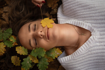 Woman Autumn Leaves Relaxation: Peaceful autumn scene, young woman resting on leaves, enjoying nature's tranquility.