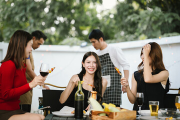 Three young women enjoying red wine together at a cozy outdoor party, smiling and relaxing with friends in a warm, festive atmosphere.