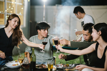 Group of friends having a fun backyard barbecue party at night, grilling food, chatting, and enjoying drinks together in a joyful atmosphere.