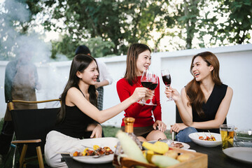 Three young women enjoying red wine together at a cozy outdoor party, smiling and relaxing with friends in a warm, festive atmosphere.
