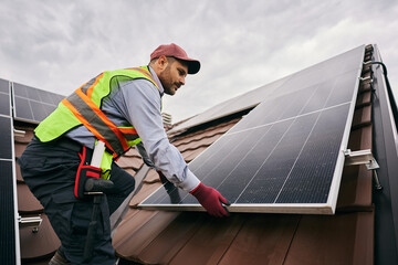 Male technician installing photovoltaic solar panels on roof.