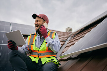Happy worker talking on cell phone during solar panels maintenance of roof. © Drazen