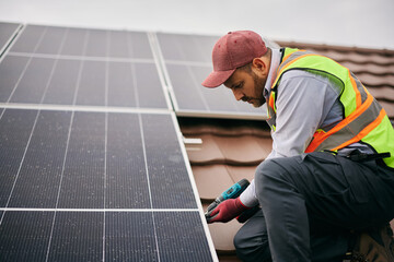 Male worker installing photovoltaic solar panels on roof.
