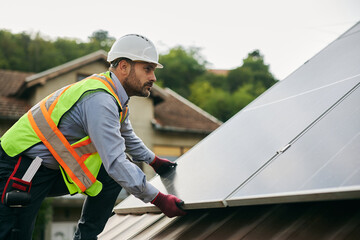 Male worker installing photovoltaic solar modules on rooftop.
