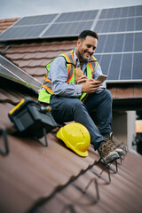 Happy engineer having a sandwich while using mobile phone on roof.