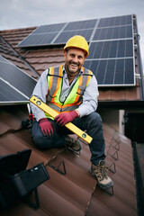 Happy maintenance engineer working on solar panel system on roof and looking at camera. © Drazen