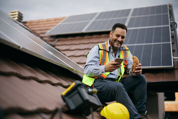 Happy roofer using smart phone while having lunch break during solar panel installation. © Drazen