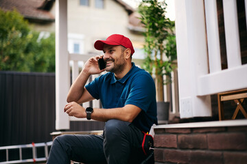 Happy home repairman talking on cell phone at work.
