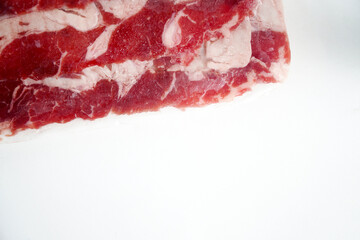 A close-up, top-down view of thinly sliced raw beef, showing the rich red color and intricate marbling of fat. The fresh meat is ready for cooking, representing healthy food and a delicious meal.
