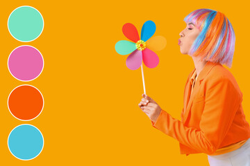 Beautiful young happy woman in colorful wig with toy windmill blowing on yellow background