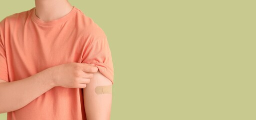 Young man with applied medical patch on green background with space for text, closeup. Immunization concept