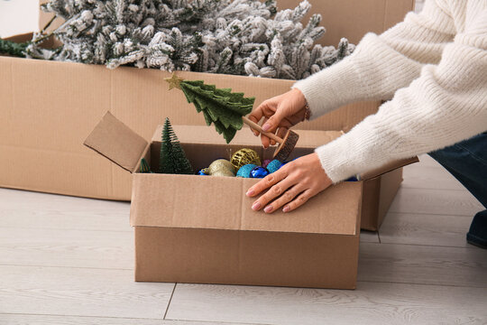 Woman putting Christmas toys in  cardboard box at home, closeup